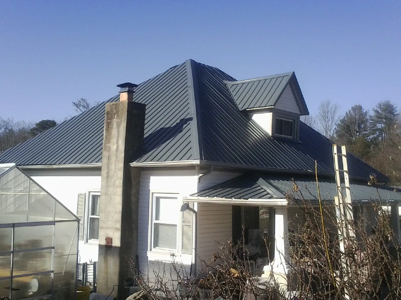Dark blue standing seam metal roof on a white farmhouse with dormer — Slate & Tile Roof Repair by Roofing Brothers in Fontana