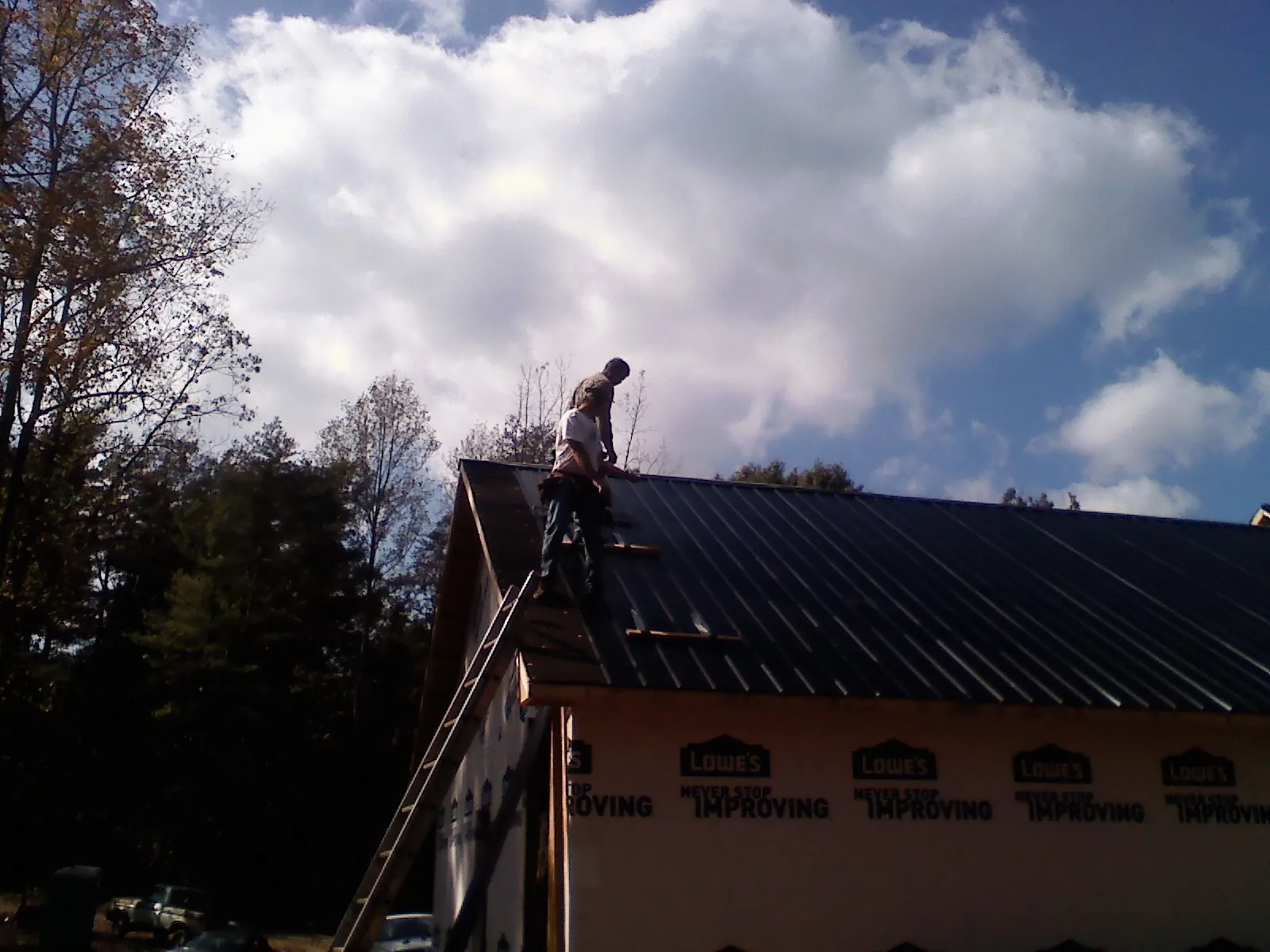 Roofer fastening dark metal panels high against a cloudy sky, from a Roof Inspection job in Fontana